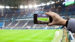 Fan hand with smartphone photographing footbal game